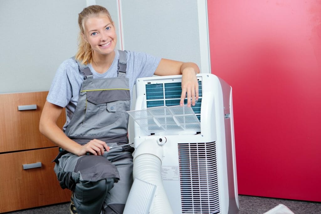 Technikerin sitzt neben Mobiler Monoblock Klimaanlage mit geöffnetem Luftauslass