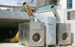 Mobile Lufterhitzer Edelstahl stehen vor Gebäude und transportieren warme Luft mittels Gebläse und gelber Schläuche in das Haus